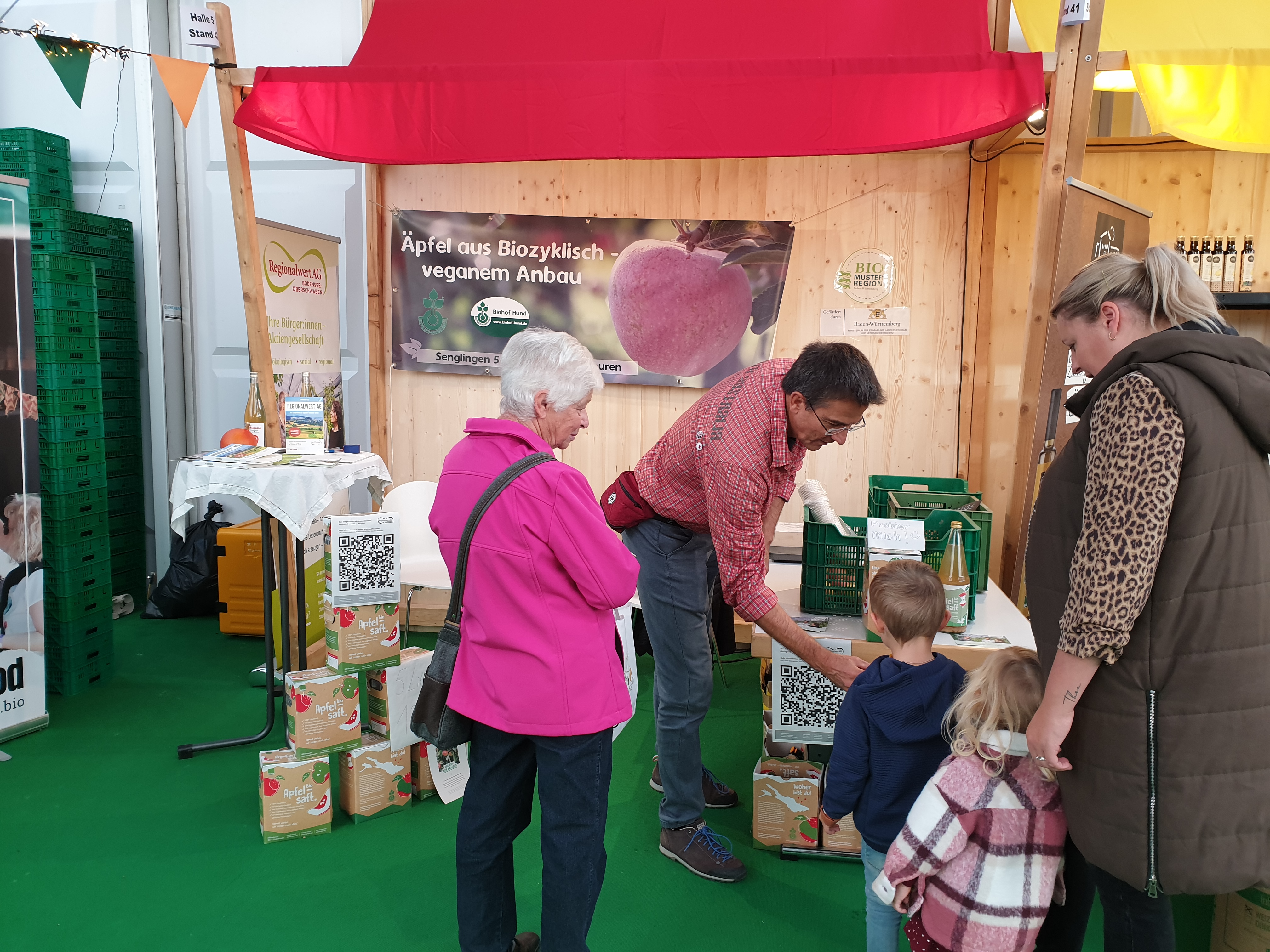 Man sieht den Stand des Biohofs Hund. Stefan Schwarz von der Regionalwert AG gibt einem kleinen Besucher Apfelsaft zum Probieren